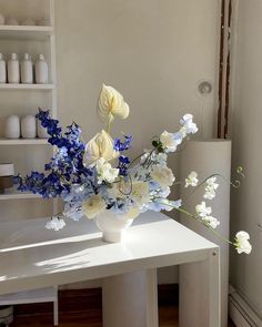 a white vase filled with blue and white flowers on top of a table next to shelves