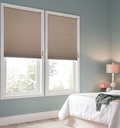 a bedroom with blue walls and two windows that have roman shades on the window sill