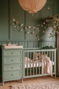 a baby crib in a green room with pink and white flowers hanging from the ceiling