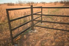 a fence in the middle of a field with dry grass and weeds growing on it