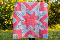 a woman holding up a pink and blue quilt