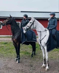 two people are riding horses in front of a red barn and one is wearing a blue jacket