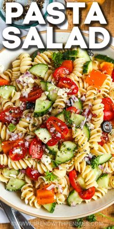 pasta salad with tomatoes, cucumbers and other vegetables in a white bowl on a wooden table