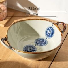 a white bowl with blue designs on it sitting on top of a wooden table next to a book