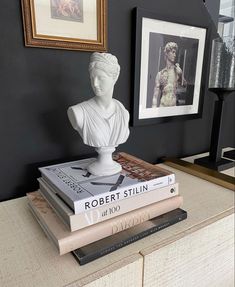 three books stacked on top of each other next to a busturine and framed pictures