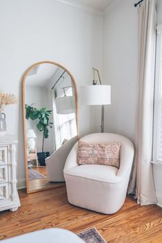 a living room with white furniture and a large mirror on the wall next to it