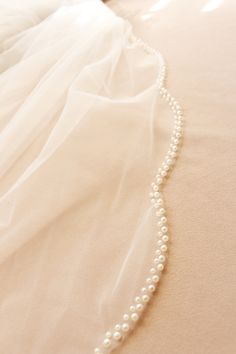 a wedding dress with a white beaded necklace on it's neckline, laying on a bed