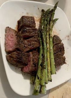 steak and asparagus in a white dish on a table with utensils