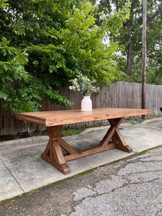 a wooden table sitting on top of a cement ground next to a fence and trees