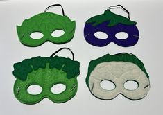 four masks with green, purple and blue designs are on a white surface next to each other