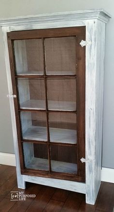 an old bookcase is painted white and has glass doors on the front, along with wood flooring