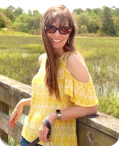 a woman standing on a wooden fence with a handbag in her other hand and smiling at the camera