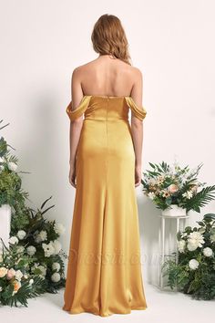 the back of a woman in a gold dress standing next to flowers and greenery