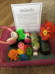 a pink container filled with toys on top of a floor next to a sign that says calm down box