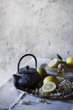 a tea kettle sitting on top of a metal tray filled with lemons and herbs