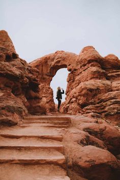 a man standing on top of a rock formation next to some rocks and stairs with an arch in the middle