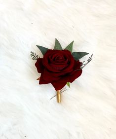 a single red rose with green leaves on a white surface, ready to be used as a boutonniere