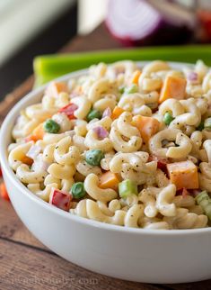 a white bowl filled with macaroni salad on top of a wooden table next to vegetables