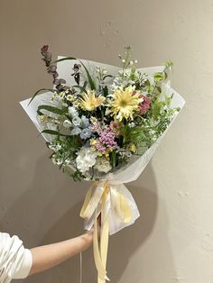 a woman holding a bouquet of flowers in her hand with the ribbon tied around it