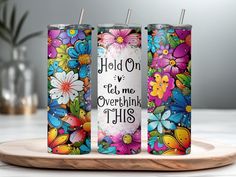 three personalized tumbles with colorful flowers and the words hold on to me overthik