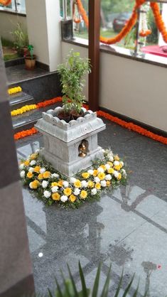 a small statue with flowers around it in the middle of a room filled with orange and white garlands