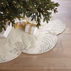 a christmas tree with presents under it on a white rug in front of a fireplace