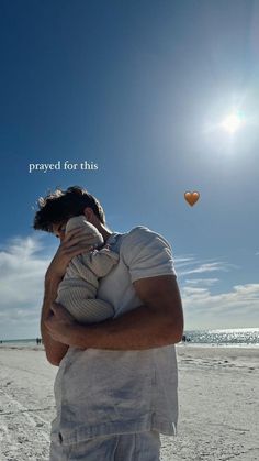 a man holding a baby while standing on top of a beach