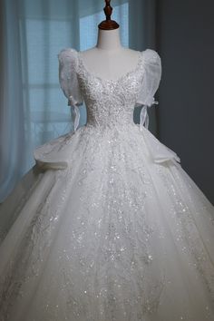 a white wedding dress on display in front of a window with sheer drapes and sequins