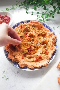 a person dipping something into a bowl of hummus on a blue and white plate