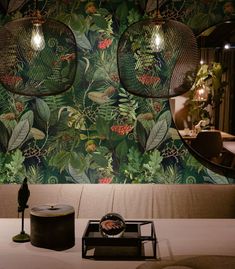 two lamps hanging from the ceiling in front of a green wall with leaves and flowers