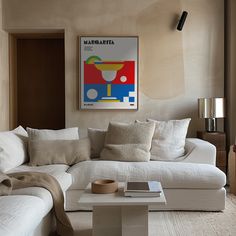 a living room with a white couch, coffee table and large poster on the wall