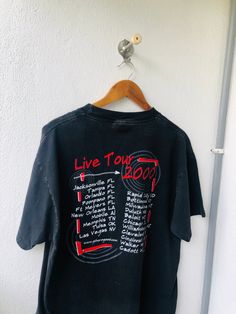 a black t - shirt with red writing on it hanging from a hanger in front of a white wall