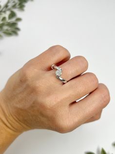 a woman's hand with a diamond ring on her left hand and green plants in the background