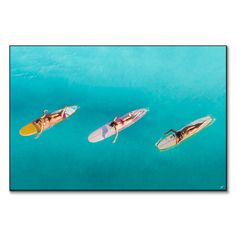 three people on surfboards floating in the blue water with one person holding a yellow board