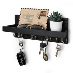 a black shelf with keys, sunglasses and mail on the wall next to a potted plant