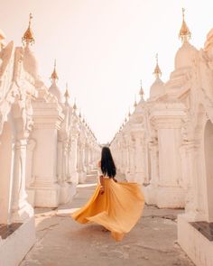 a woman in a yellow dress is walking through an old white building with arches and spires