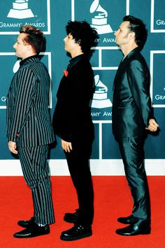 three men in black and white suits standing on a red carpet at an awards event