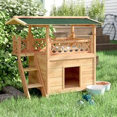 a wooden dog house in the grass with a green roof and stairs leading up to it