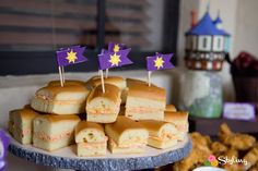 there are many desserts on the table with purple and yellow flags sticking out of them