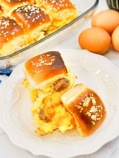 two breakfast sandwiches on a white plate next to eggs and an oven mitt in the background