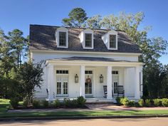 a white house with black shingles on the roof and two porches, surrounded by trees