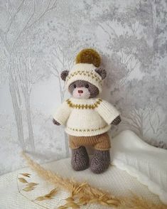 a teddy bear wearing a knitted hat, sweater and pants sitting on top of a blanket