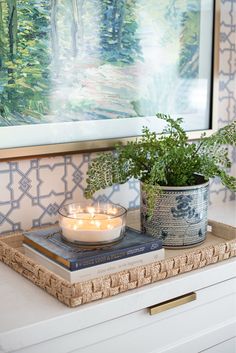 a candle and some plants are on a tray in front of a wall with a painting