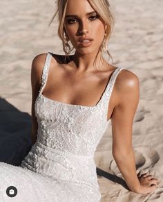 a woman sitting in the sand wearing a white wedding dress with spaghetti top and low back