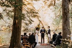 a couple getting married in the woods by the river with their wedding party around them