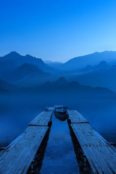 two wooden benches sitting on top of a body of water next to mountains in the distance