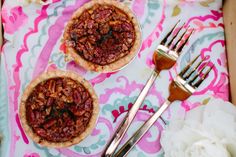 two small pies sitting on top of a pink and blue table cloth next to silverware