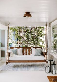 a porch swing bed with pillows on it in front of a window and potted tree