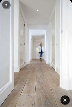 a person walking down a long hallway with white walls and wood flooring on either side