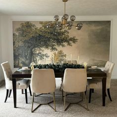 a dining room table with white chairs and a large painting on the wall behind it